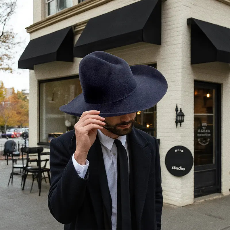 Outside a building with a black awning, a formally dressed man wore a navy blue, wide-brimmed felt cowboy hat.