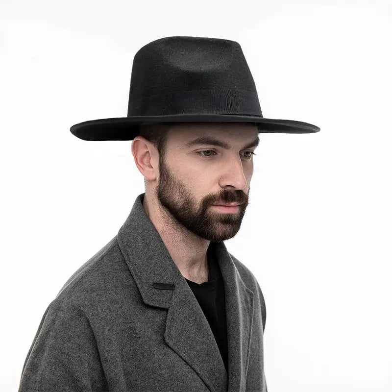 Man wearing a black wide - brimmed hat, a gray overcoat, and a black shirt, set against a plain white background