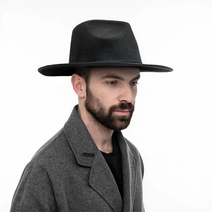 Man wearing a black wide - brimmed hat, a gray overcoat, and a black shirt, set against a plain white background